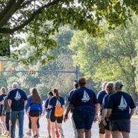 Large group of GVSU Alumni walking in a pack from Alumni House & Visitor Center to dorm buildings